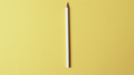 Overhead-view-of-white-crayon-with-copy-space-on-yellow-background,-in-slow-motion