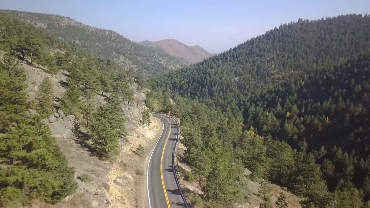 toma aérea de carro bajando por una sinuosa carretera del medio oeste de colorado con pinos en lo alto de las montañas en un día soleado y seco