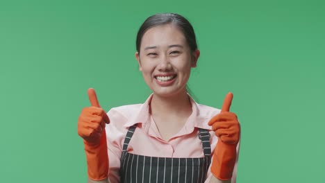 primer plano de una ama de casa asiática con un delantal sonriendo y mostrando los pulgares hacia arriba mientras está de pie en el estudio de pantalla verde