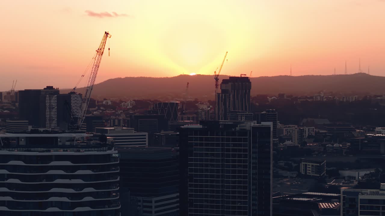 Descenso aéreo sobre el skyline de Brisbane desde Teneriffe mientras los colores del atardecer se asientan sobre la ciudad con altas grúas de construcción, CBD Queensland Australia