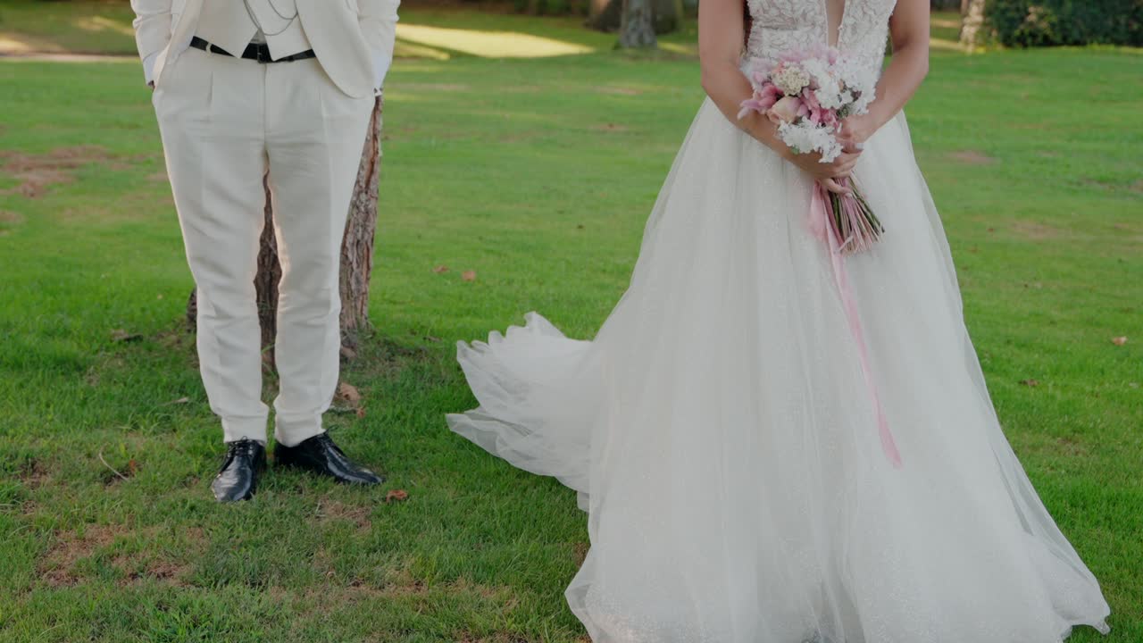 couple stands together on a lush green lawn, the bride holding a pink bouquet