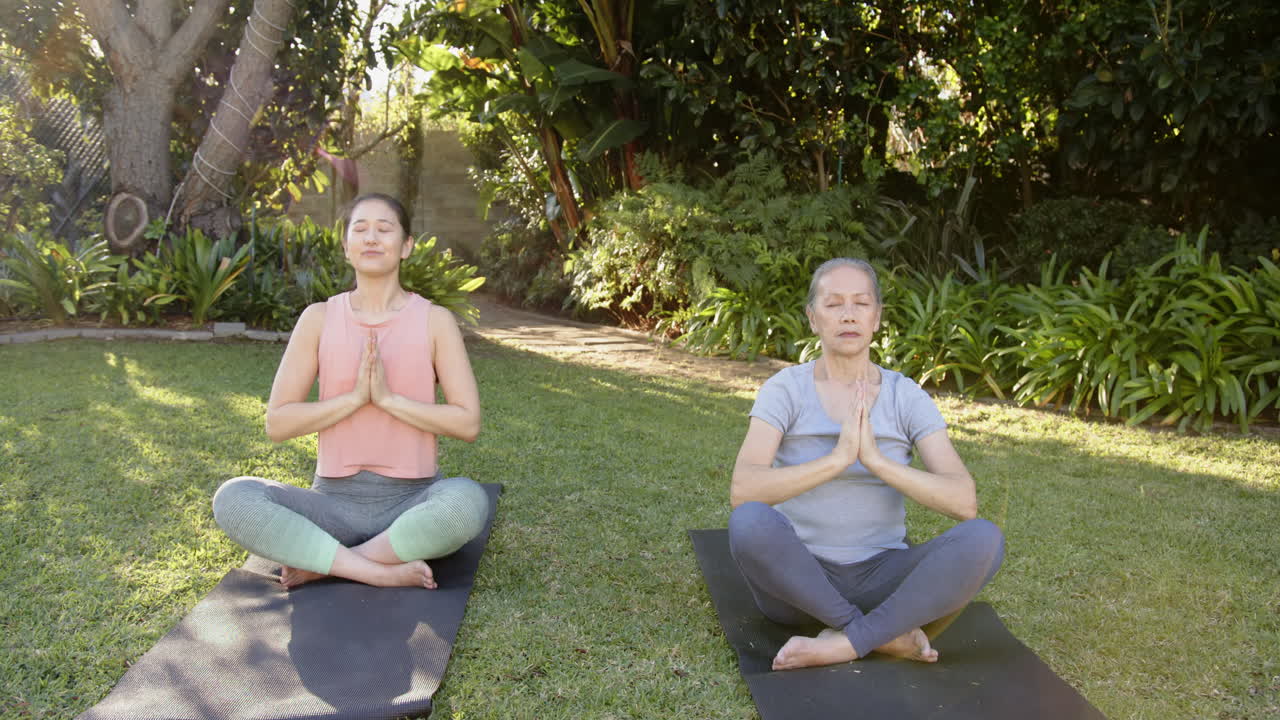 Practicing yoga, Asian grandmother and granddaughter meditating on yoga mats in garden