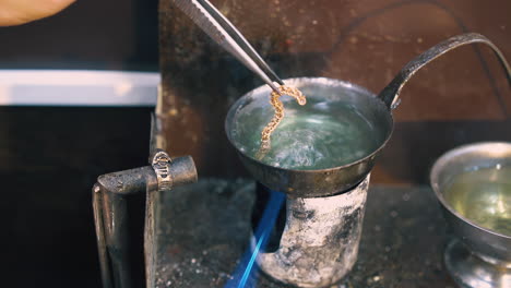 goldsmith takes chain off boiling green liquid closeup