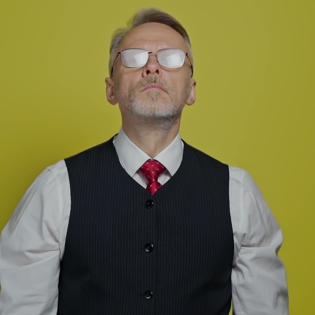 Portrait of a serious senior businessman. Mature man with grey beard in glasses standing on a yellow background and looking at camera.
