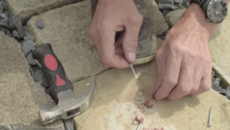 Workman hands hammering nails into nail hook cable clip on concrete floor