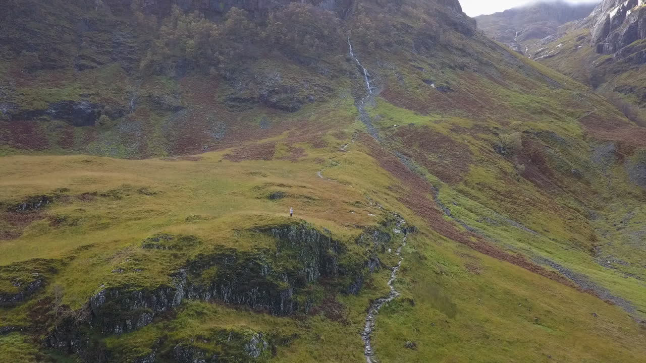 Drone in orbita su un escursionista su un promontorio roccioso che si gode la vista della valle delle Highlands.