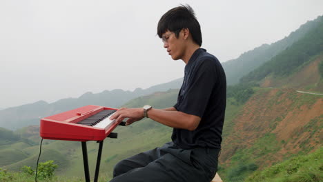 Eleganter-Südostasiatischer-Mann,-Der-Im-Dschungel-Auf-Einem-Hügel-Klavier-Spielt