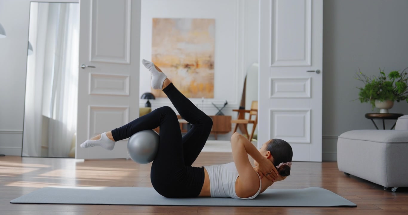 Giovane donna che esegue esercizi per il core con la palla da Pilates a casa