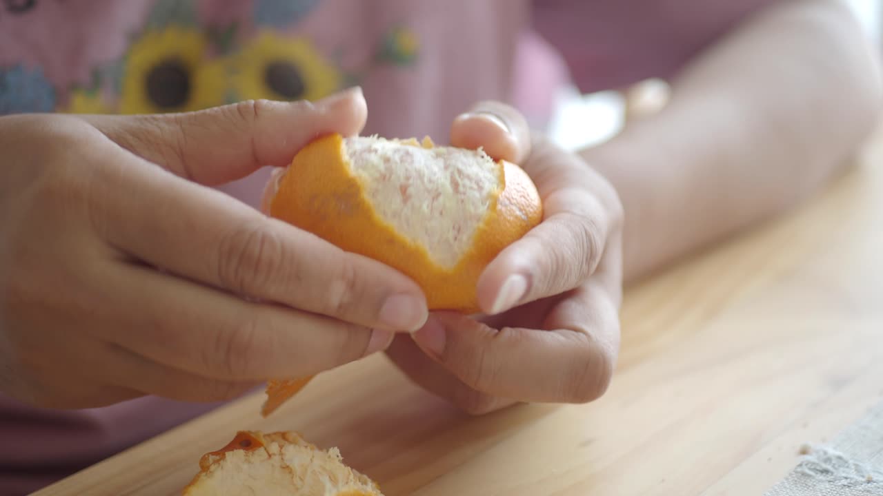 Close-up of Hands Peeling a Fresh Orange on a Wooden Table