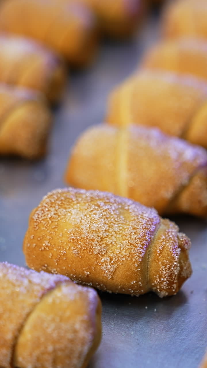 Ready-made croissants coated with sugar on the baking sheet. Little sweet desserts manufactured at bakery. Close up. Vertical video