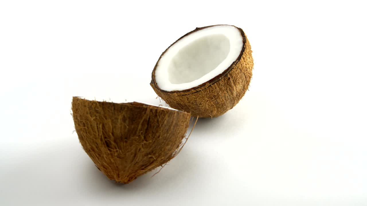 coco tropical maduro dividido en dos mitades girando sobre un fondo blanco. frutas tropicales, en bucle
