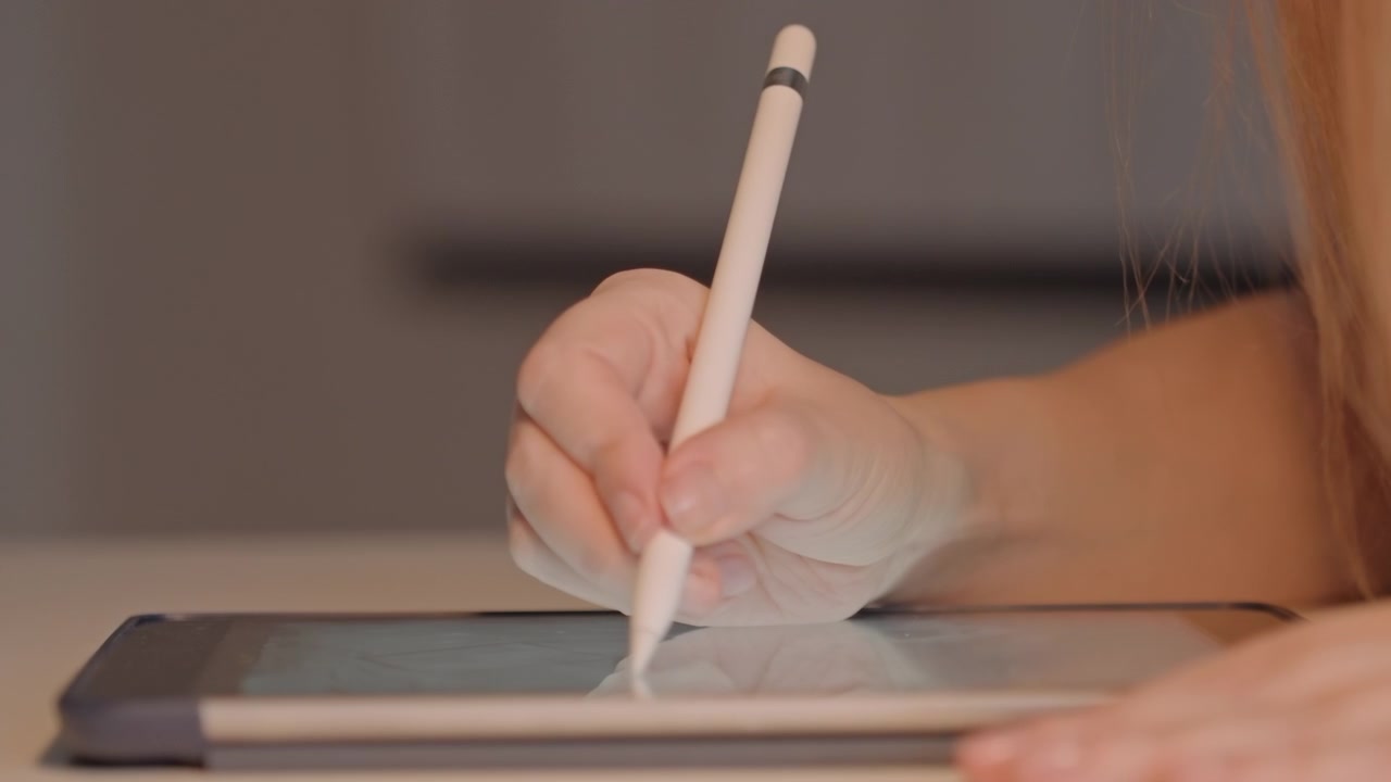 Close-up de mão segurando e movendo uma caneta stylus branca. A interação envolve desenhar ou escrever com leves variações. O fundo é de cor neutra, em ambiente interno, e o foco permanece fixo.