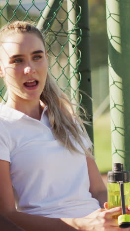 video of happy diverse female tennis players sitting, talking and resting after match