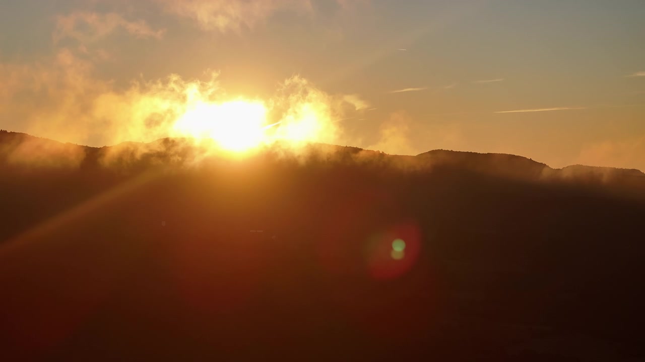 Golden sunrise over mountain ridge with orange sky and hillside mist