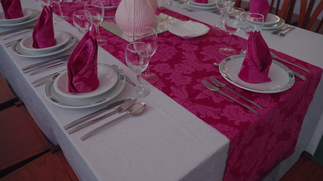 Carefully arranged wedding table with bright pink napkins and glassware on white linen