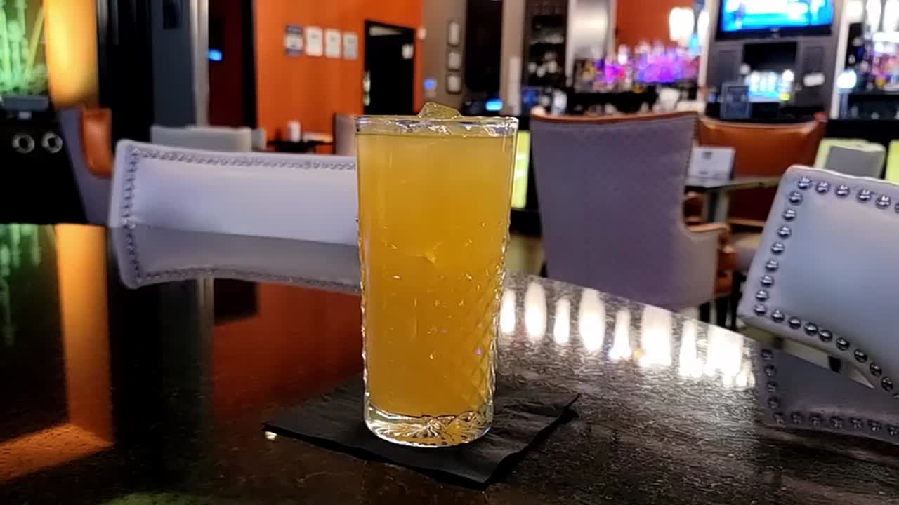 zoom hacia afuera de un refrescante jugo de naranja recién exprimido helado servido en una taza de vidrio con un moderno fondo de club nocturno sin nadie a la vista aceptar pantallas de televisión y una pantalla de caja registradora en movimiento