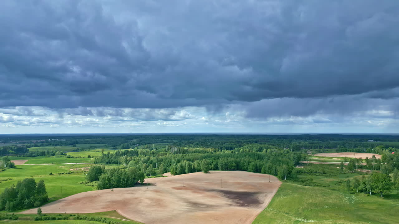 Eine Drohnenaufnahme schwenkt von bedeckten Wolken hinab auf grüne Bäume und Gras