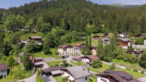 aerial approaching shot of apartment buildings in swiss village at sunny day. green growing mountains in background. laax, switzerland