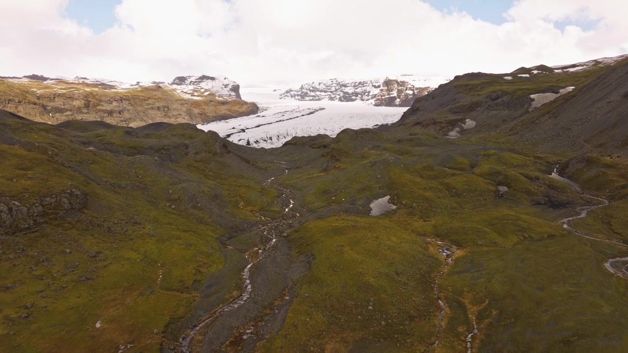 Vista aerea di Sólheimajökull, Islanda, che mostra un paesaggio aspro con colline verdi e una valle glaciale in lontananza.