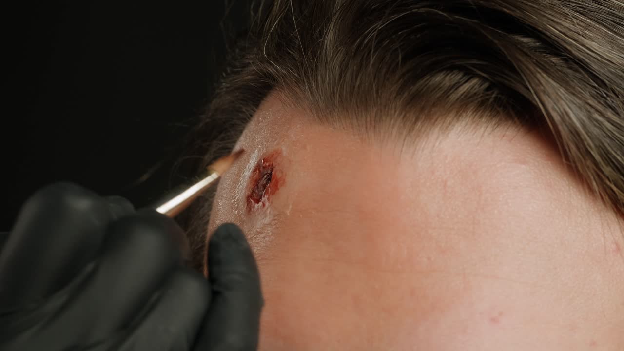 Make up artist making scars and bullet shot forehead headshot with fake blood man in theater with paint and glue, actors sfx cinema make up, close-up. Mens fashion, halloween style. making old guy.