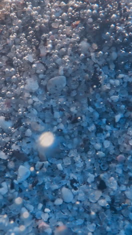 dark dirt pieces fall down on sea bottom covered with small pebbles in transparent water. thin threads with air bubbles waving by flow underwater