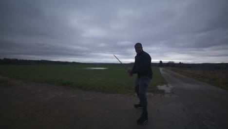 Modern-Black-Swordsman-Warrior-Awaiting-Battle-Opponent-in-Open-Field-Under-Grey-Sky,-Europe,-4K-|-Muscular,-Intimidating,-Shadow,-Figure,-Blurry,-Dark-Clothes,-Powerful,-Tense,-Stance,-Slash,-Swing