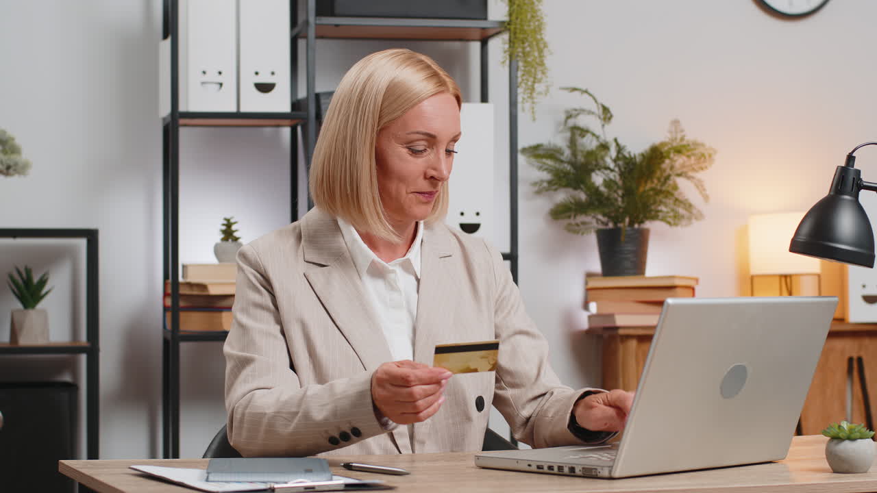 зрелая бизнесменка, использующая банковскую кредитную карту и ноутбук для платежей за покупки в интернете в домашнем офисе