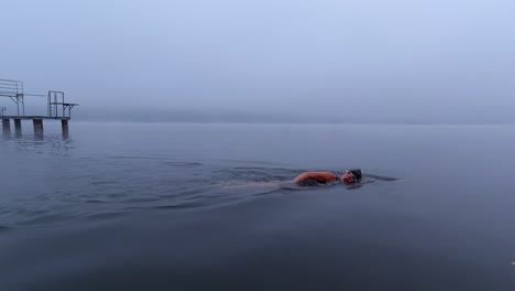 woman open-water swimming in winter in a foggy lake