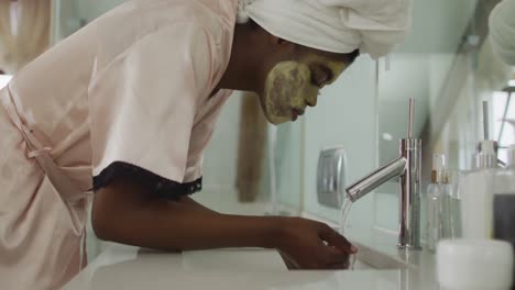 African-american-attractive-woman-washing-off-face-mask-in-bathroom