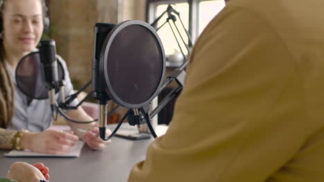 young man and woman sitting at a table with microphones while they recording a podcast 1