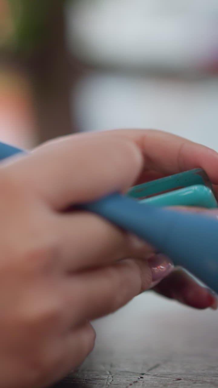 Primer plano de unas manos sujetando una paleta de contorno y un pincel, un suave barrido por la bandeja de colorete, unas uñas rosas brillantes agarrando un compacto turquesa, la superficie de una mesa de madera y un suave fondo bokeh crean un ambiente tranquilo de cuidado personal