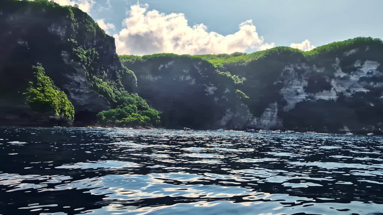 View from the water of green-topped cliffs and rocky shoreline at Manta Point, Nusa Penida, Indonesia