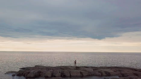 man celebrates with elation standing on rocks looking out to empty sea horizon