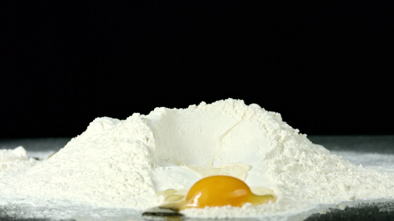 Egg Being Cracked into Some Flour, Against a Black Background
