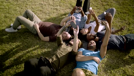 smiling young people using smartphones while lying on blanket