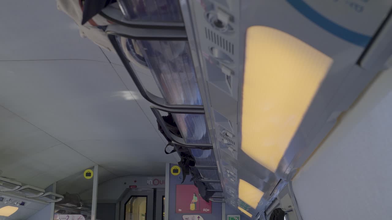 Modern train interior with overhead lights and bags stored in luggage racks