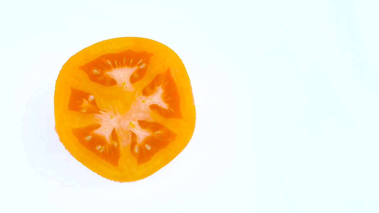 색 바탕에 고립 된 회전 테이블에 회전하는 물방울이있는 반 오렌지 노란색 토마토의 위쪽 의 절반 프레임.