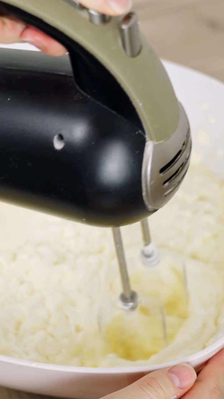 Hand mixer blending creamy batter, whipping ingredients in bowl, baking preparation, cooking process, kitchen activity