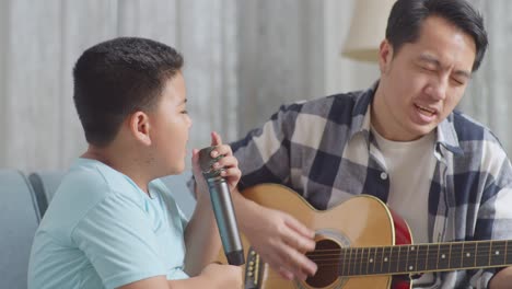 close up of happy asian father and son celebrating for being able to play the guitar and singing together on sofa at home