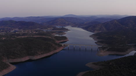 Drone-panning-around-large-river-with-a-bridge,-revealing-beautiful-landscape-and-a-large-river-in-Spain