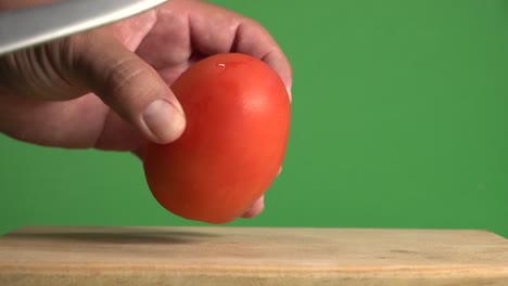 a hand horizontally slicing through a tomato on a chroma background