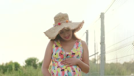 una chica embarazada camina por la carretera después de la lluvia con un sombrero y un vestido