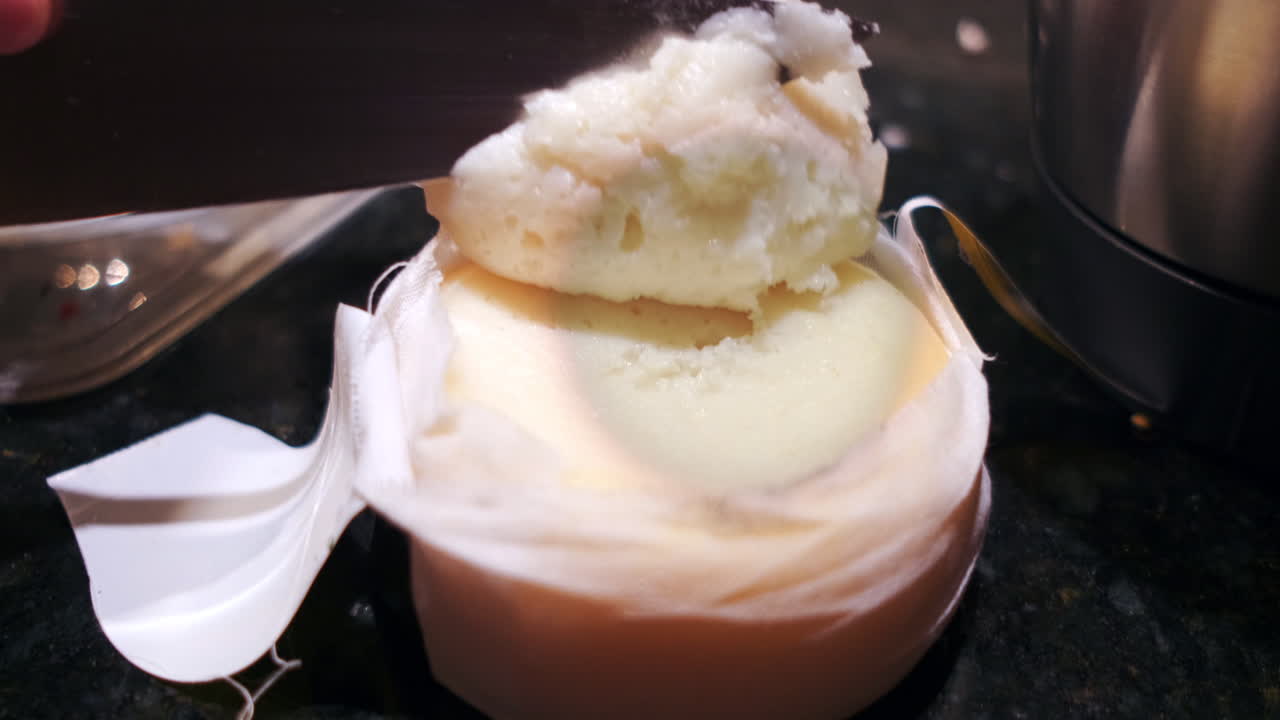 Close up shot of person cutting famous creamy Portuguese cheese with knife inside kitchen. Slow motion