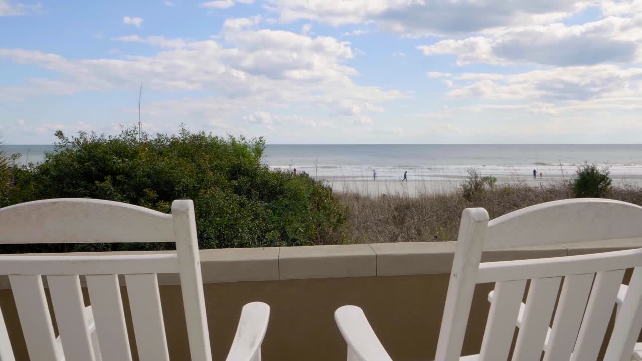 two rocking chairs gently move on balcony with view over the sea, slow motion
