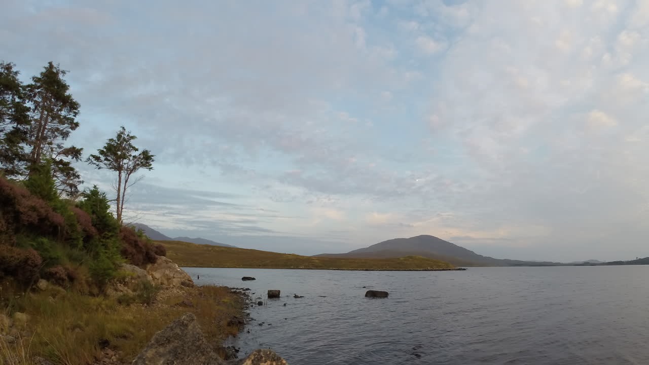 Timelapse pan left across of Connemara coastline, shifting clouds, rippling water, and dynamic light changes under soft cloudy sky