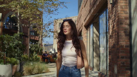 gorgeous girl exploring city street. brunette tourist walking on green district.