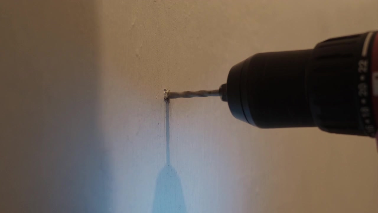 Close-up static shot of a power drill boring into an interior wall during home repair with visible dust and tool movement