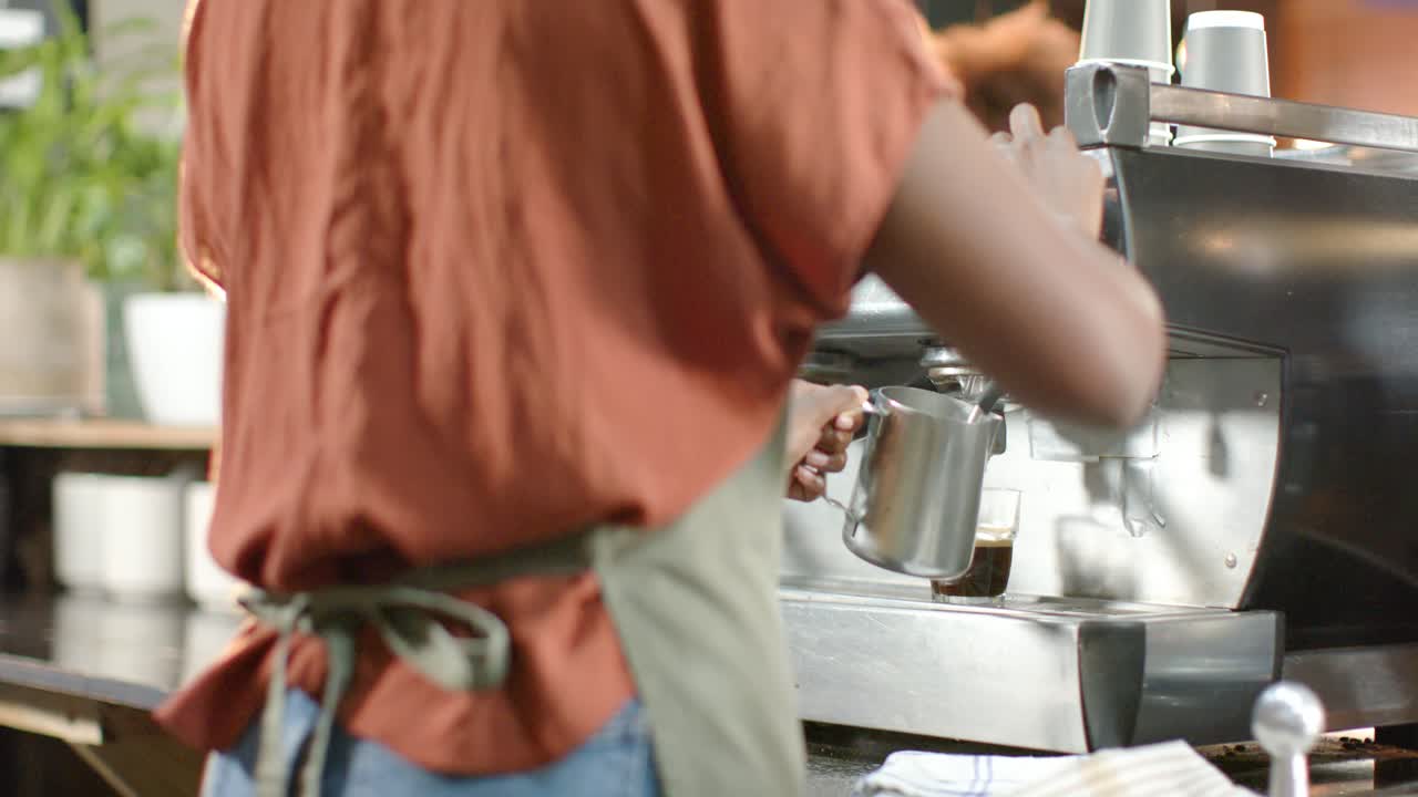 Un barista accende la lancia vapore, montando il latte in una lattiera metallica al bancone del bar per creare la schiuma.