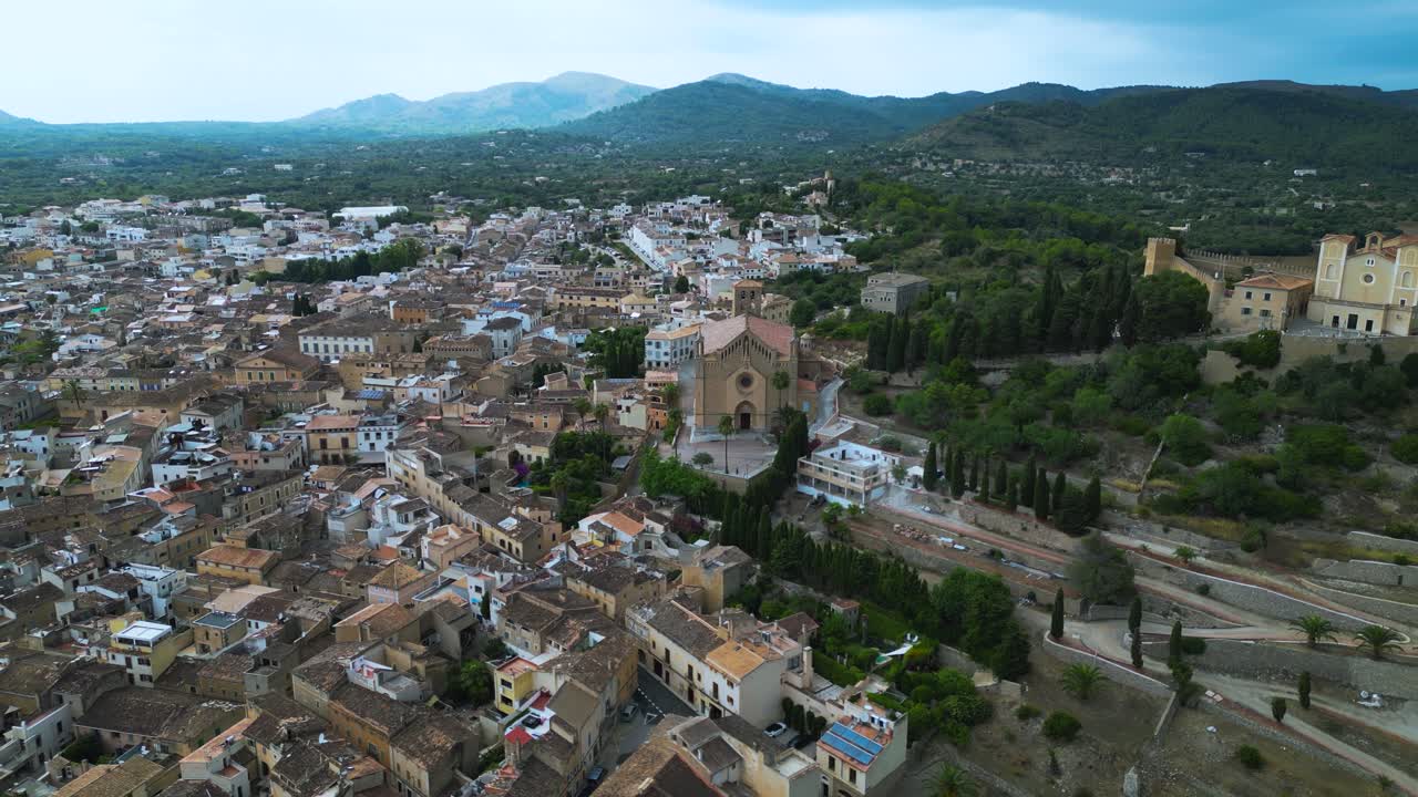 Ampio panorama aereo di Arta con la chiesa simbolo circondata da colline e isolati urbani, ripresa all'indietro. Maiorca, Spagna