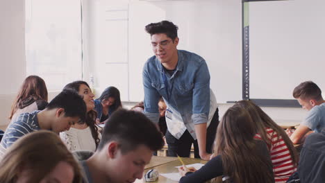 male high school teacher talking to student sitting at desks during lesson